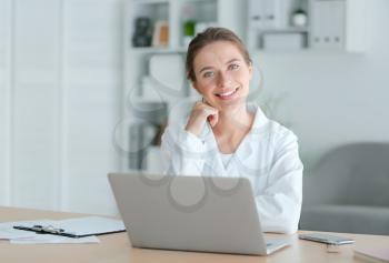 Female doctor with laptop sitting at table in clinic�