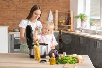 Woman and her little daughter using modern multi cooker in kitchen�