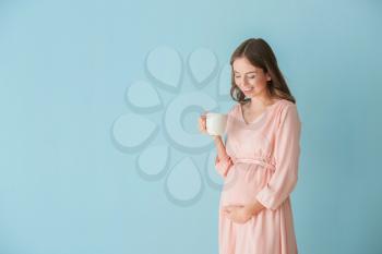 Beautiful pregnant woman with cup of tea on color background 