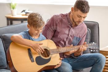 Father teaching his little son to play guitar at home�
