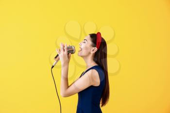 Beautiful young female singer with microphone on color background�