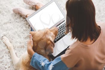 Beautiful young woman with cute dog using laptop at home�