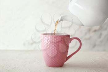 Pouring of hot tea from teapot into cup on table�