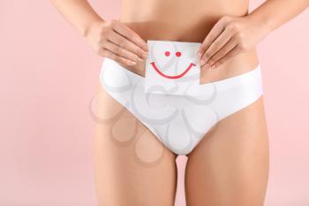 Young woman holding paper with drawn happy emotion on color background. Gynecology concept�