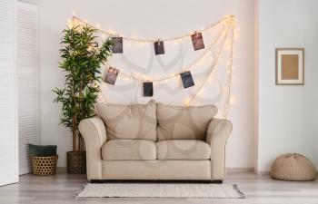 Interior of room with sofa and glowing garland with photos on white wall�