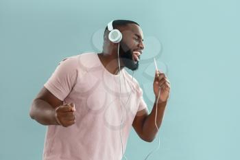African-American man listening to music and singing on color background�