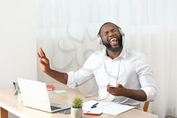 Emotional African-American man listening to music in office�