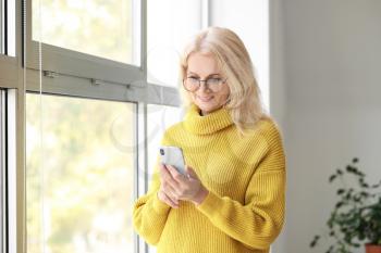 Portrait of beautiful mature woman with mobile phone near window�