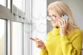 Portrait of beautiful mature woman talking by phone near window�