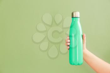 Female hand with sports water bottle on color background�