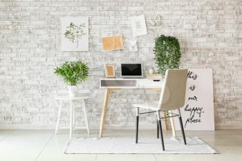 Comfortable workplace with mood board and laptop near brick wall�