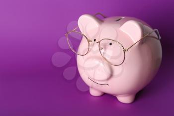 Piggy bank with eyeglasses on color background�