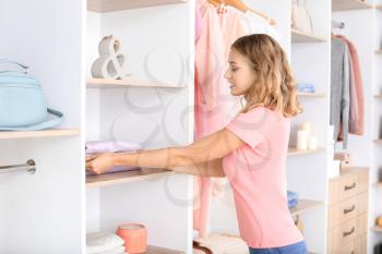 Woman putting clean clothes onto shelf at home�