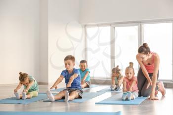 Little children practicing yoga with instructor in gym�