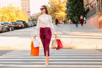 Beautiful young woman with shopping bags crossing road�