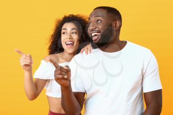 Portrait of happy African-American couple pointing at something on color background�