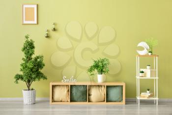 Stylish furniture with pillows and houseplants near color wall in room�