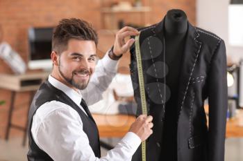 Young tailor taking measurements of male jacket on mannequin in atelier�
