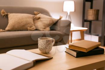 Books with cup of coffee on table in room at night�