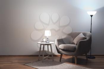 Cozy armchair with table and glowing lamps at night�