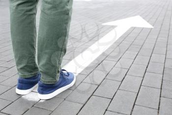 Young man standing on road with arrow marking. Concept of choice�