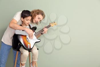 Man teaching his son to play guitar on color background�