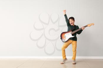 Emotional little boy playing guitar near light wall�