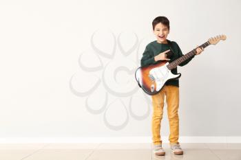 Little boy playing guitar near light wall�