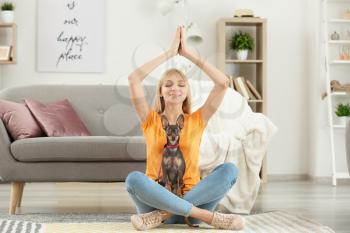 Beautiful young woman with cute toy terrier dog meditating at home�