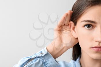 Young woman with hearing problem on light background�