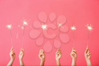 Female hands with Christmas sparklers on color background�