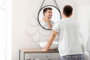 Handsome young man looking in mirror after shaving at home�