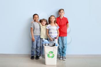 Little children and container with trash near color wall. Concept of recycling�