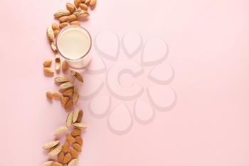 Glass of tasty almond milk and nuts on color background�