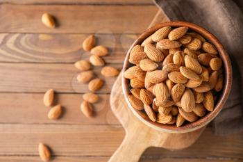 Bowl with tasty almonds on wooden table�