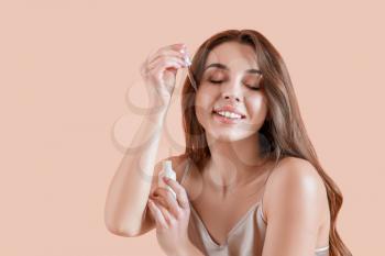 Beautiful young woman applying serum onto her skin against color background�