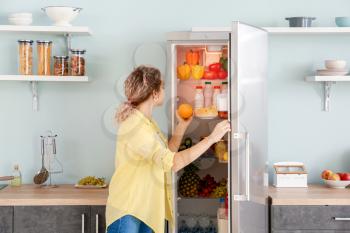 Woman choosing food in modern fridge at home�