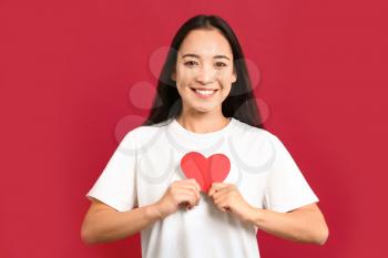 Beautiful young Asian woman with paper heart on color background�