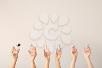 Female hands with different perfume bottles on grey background�