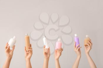 Female hands with different cosmetic products in bottles on grey background�