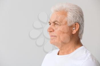 Mature man with hearing aid on light background�