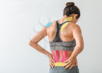 Sporty woman with physio tape applied on back against light background�
