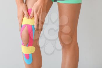 Sporty woman with physio tape applied on knee against light background, closeup 