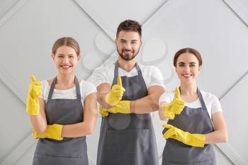 Team of janitors showing thumb-up gesture on grey background�