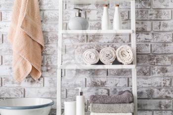 Clean towels with cosmetics on shelves in bathroom�
