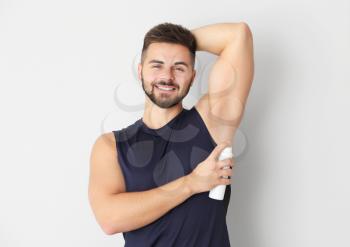Handsome young man using deodorant on light background�