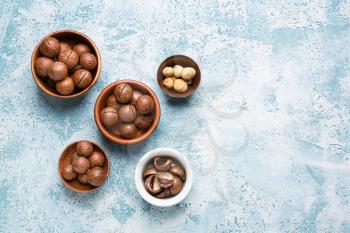 Bowls with macadamia nuts on color background�