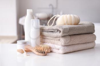 Stack of towels, cosmetics, loofah and brushes on table in bathroom�