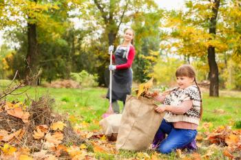Mother and daughter cleaning up autumn leaves outdoors�
