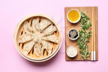 Bamboo steamer with tasty Japanese gyoza and sauces on color background�